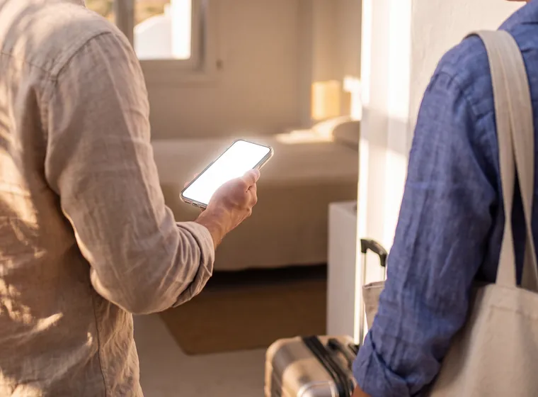 A guest at the door of a bright room at twenty to four, holding a phone open on the Stay Hub, no login needed.